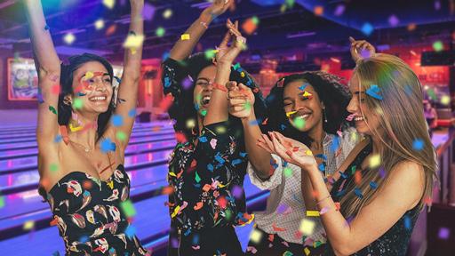 A group of teenagers on the bowling lanes with confetti and neon lanes behind them. 