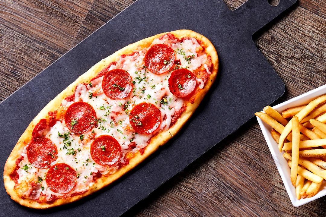 Pepperoni flatbread on a black stone with french fries.