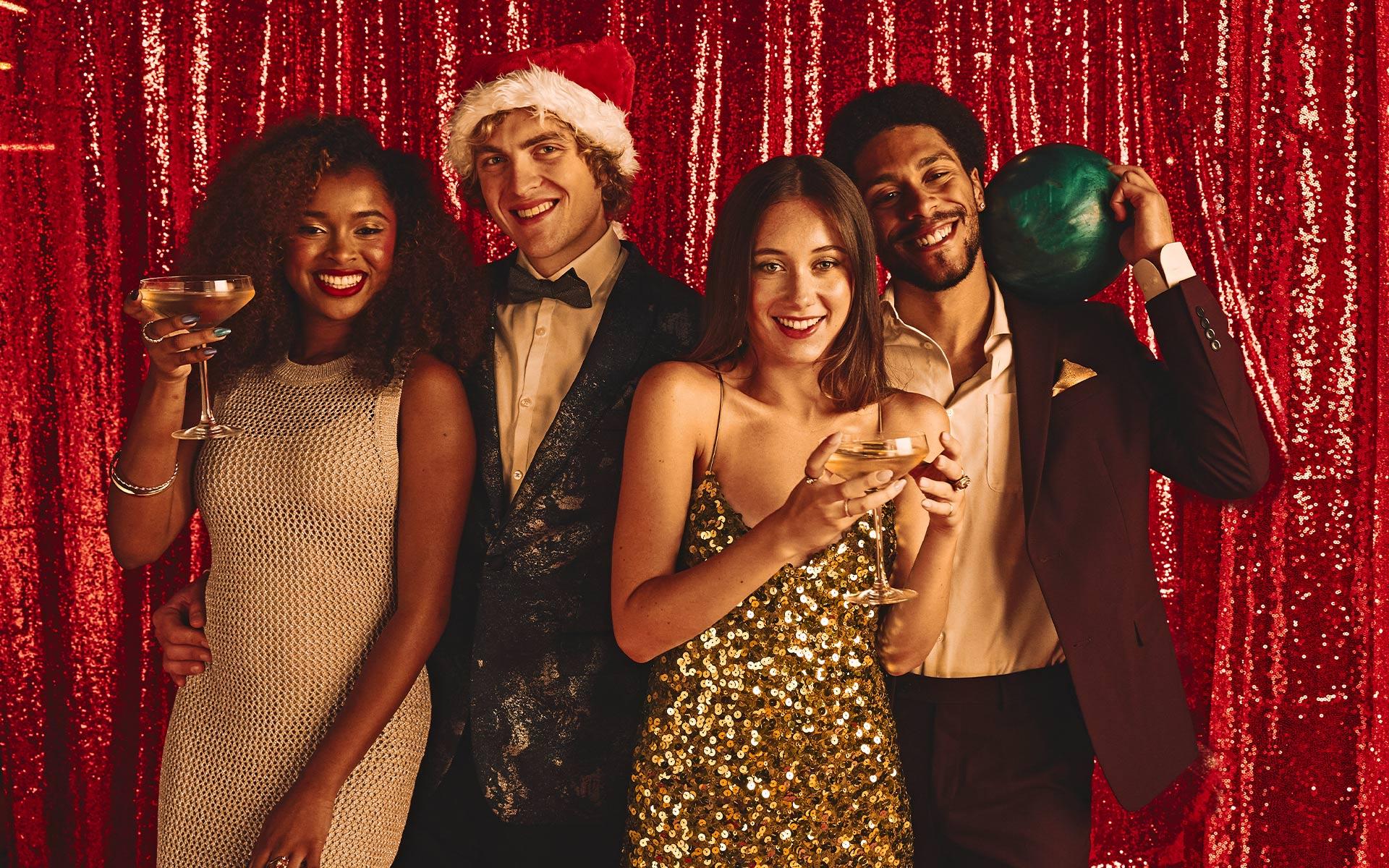 Four friends dressed up in holiday attire in front of a red sequence backdrop 