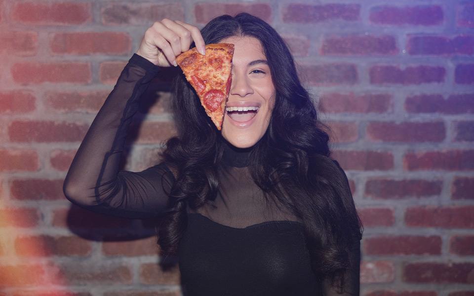 A girl holding up a slice of pizza while laughing and having fun at a birthday party with her friends.