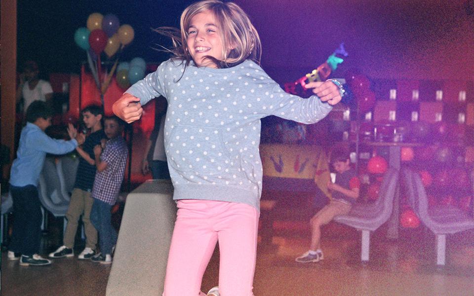 A girl jumping up and down, excited to be bowling at a kid's birthday party. 