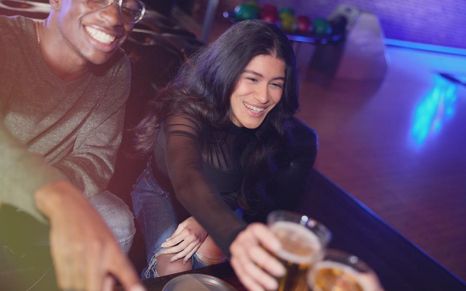 A girl toasting beer with friends at a bowling alley. 