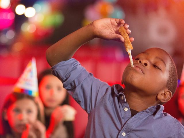 A kid eating a mozzarella stick, enjoying a kid's birthday party. 